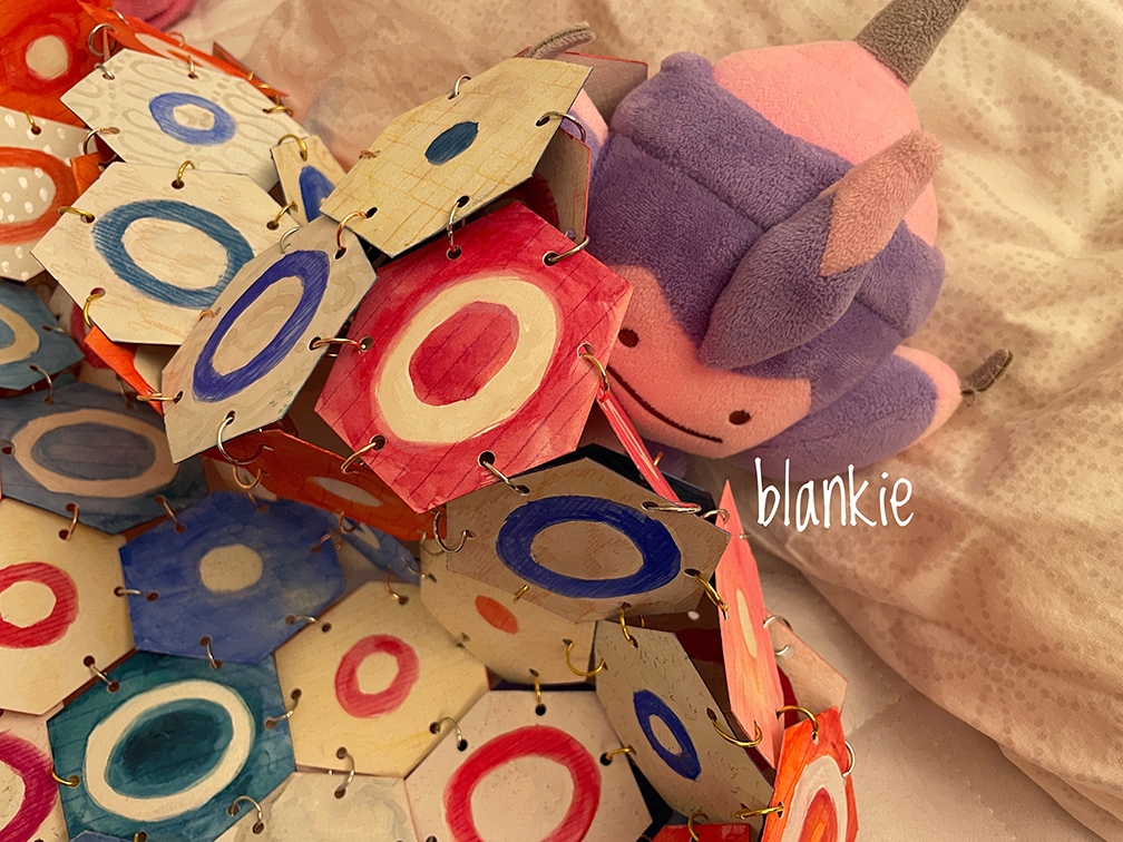 Paper hexagon blanket covering stuffed animal in bed.
